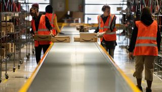 Amazon workers load boxes onto a conveyor belt in a warehouse in France.
