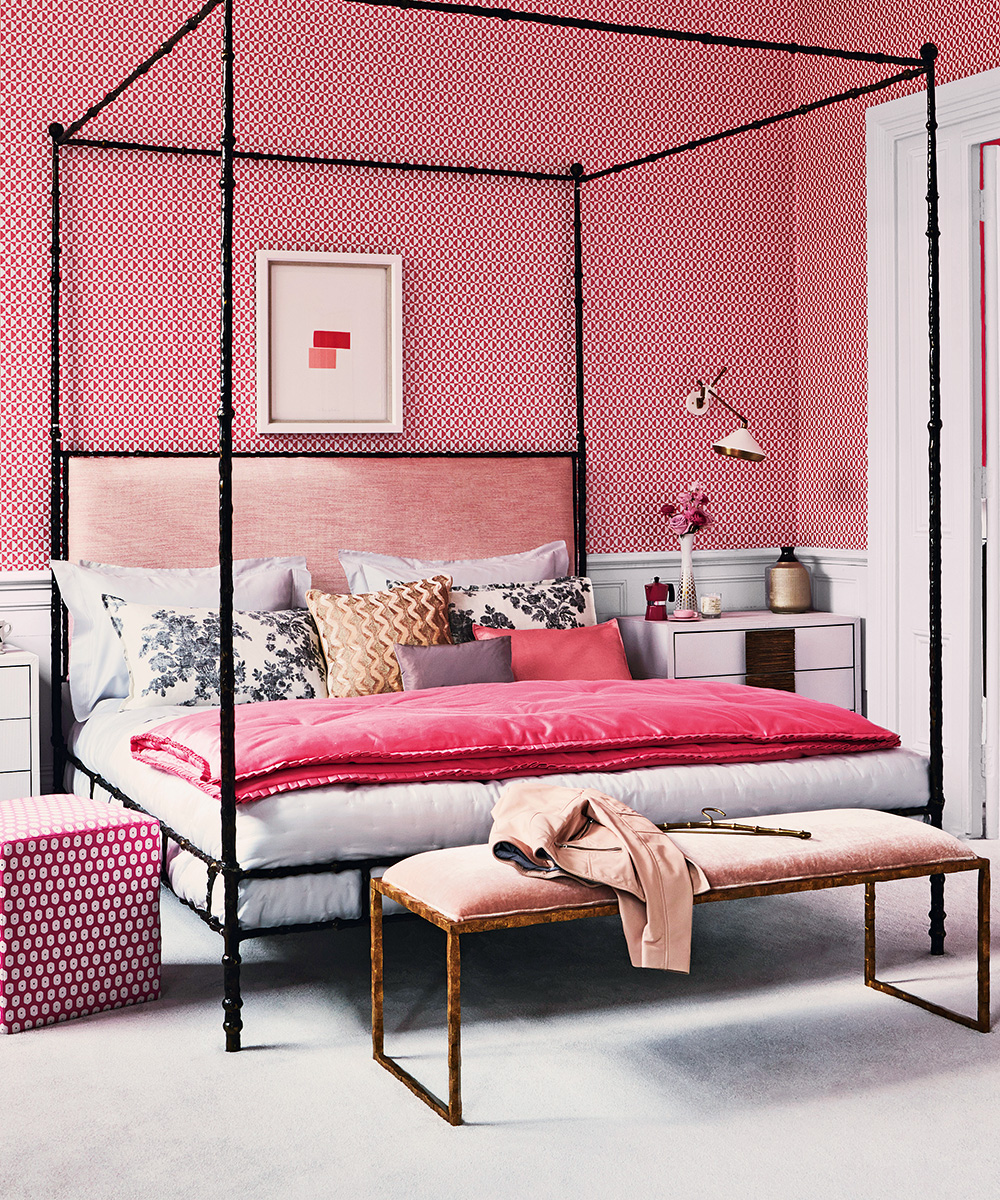 Pink patterned bedroom wallpaper behind a black four poster bed, with pink velvet accessories and soft white carpets.