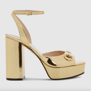 a pair of gold metallic gucci sandals in front of a plain backdrop