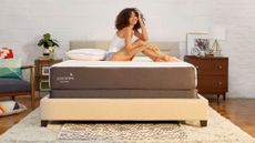 Best mattress under $1,000: A woman with curly hair smiles as she sits on the Cocoon by Sealy Chill mattress