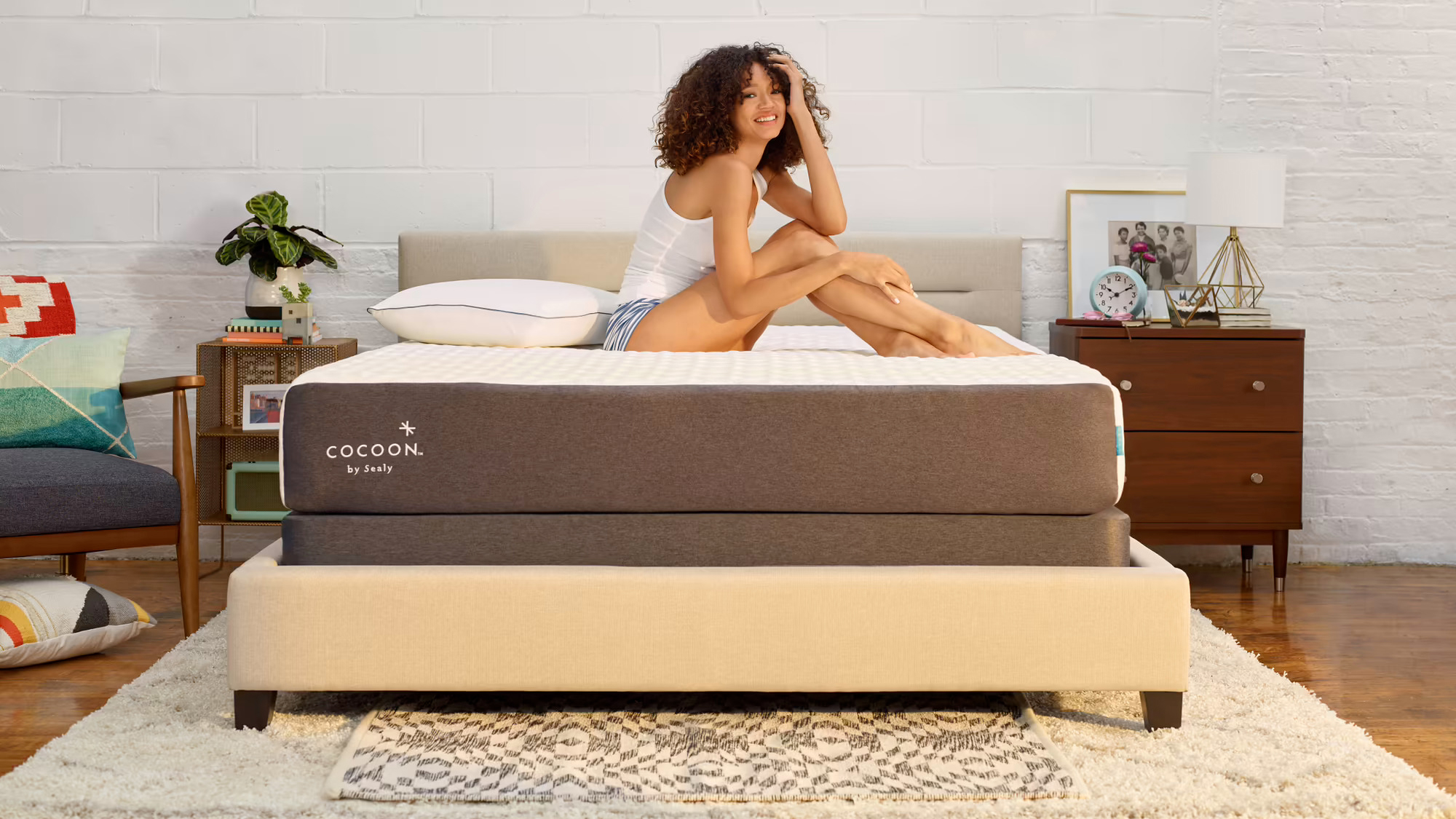 A woman with curly hair sits on the Cocoon by Sealy Chill mattress