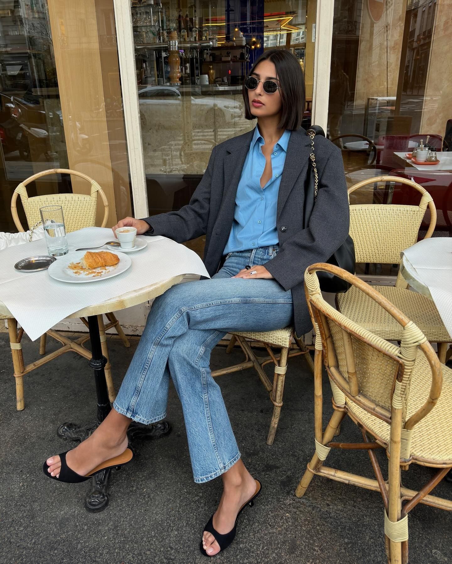 A French woman sitting outside of a cafe eating a croissant and drinking a coffee