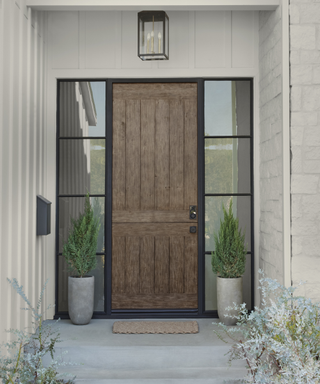 A gray house exterior with a wooden doorway and shrubs.