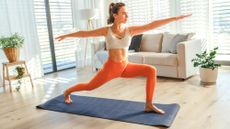 Woman performing Warrior II yoga pose during yoga workout on yoga mat in a light and sunny home