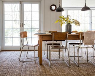 Textured brown carpet in dining room, dark wood dining table, wood and metal dining chairs, low hanging pendant lights, flowers on table
