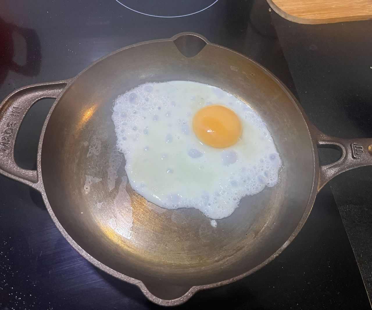 A small bronze colored cast-iron skillet with a single fried egg inside.