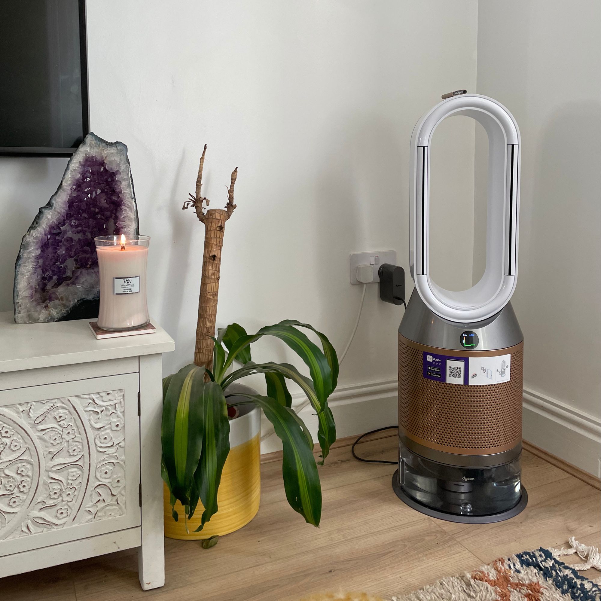 Dyson air purifier standing next to a palm plant and a candle