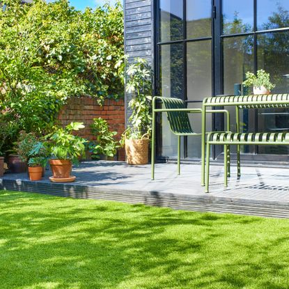 a sunny garden with an artificial grass lawn and a metal table and chairs