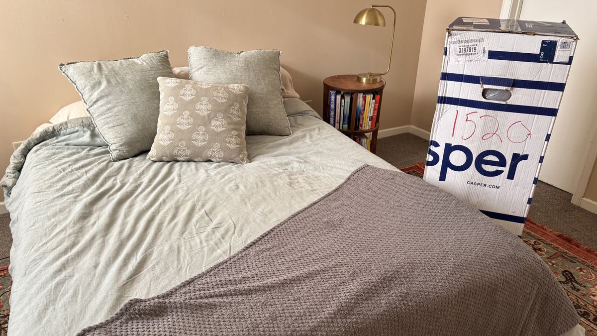 Casper One Mattress dressed in sheets and a comforter, with the box it arrived in next to it