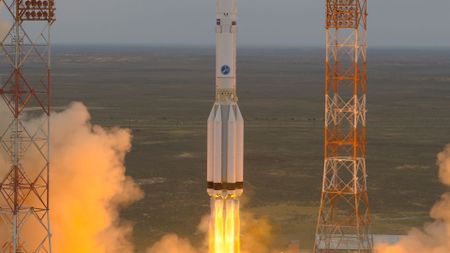 a white rocket with side mounted boosters launches from a desert launch pad