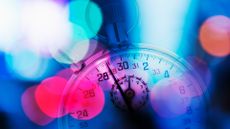 A macro photo of a stopwatch, framed and vignetted by bright light bokeh, in pinks, blues, and oranges, to represent latency.