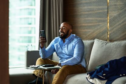 Man sitting on sofa at home smiling and using smartphone