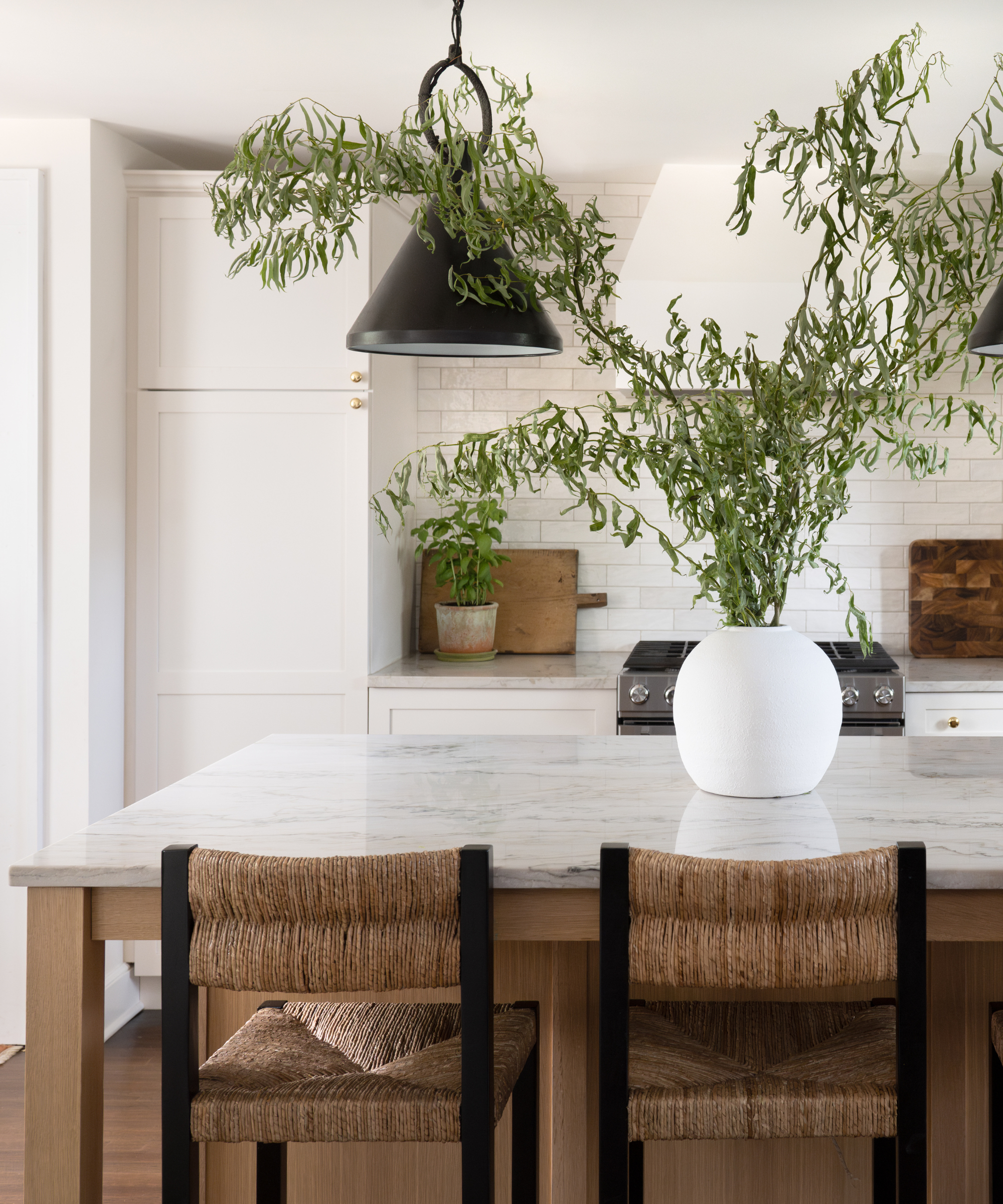 A greige kitchen with a marble island and wicker chairs, and a large potted plant