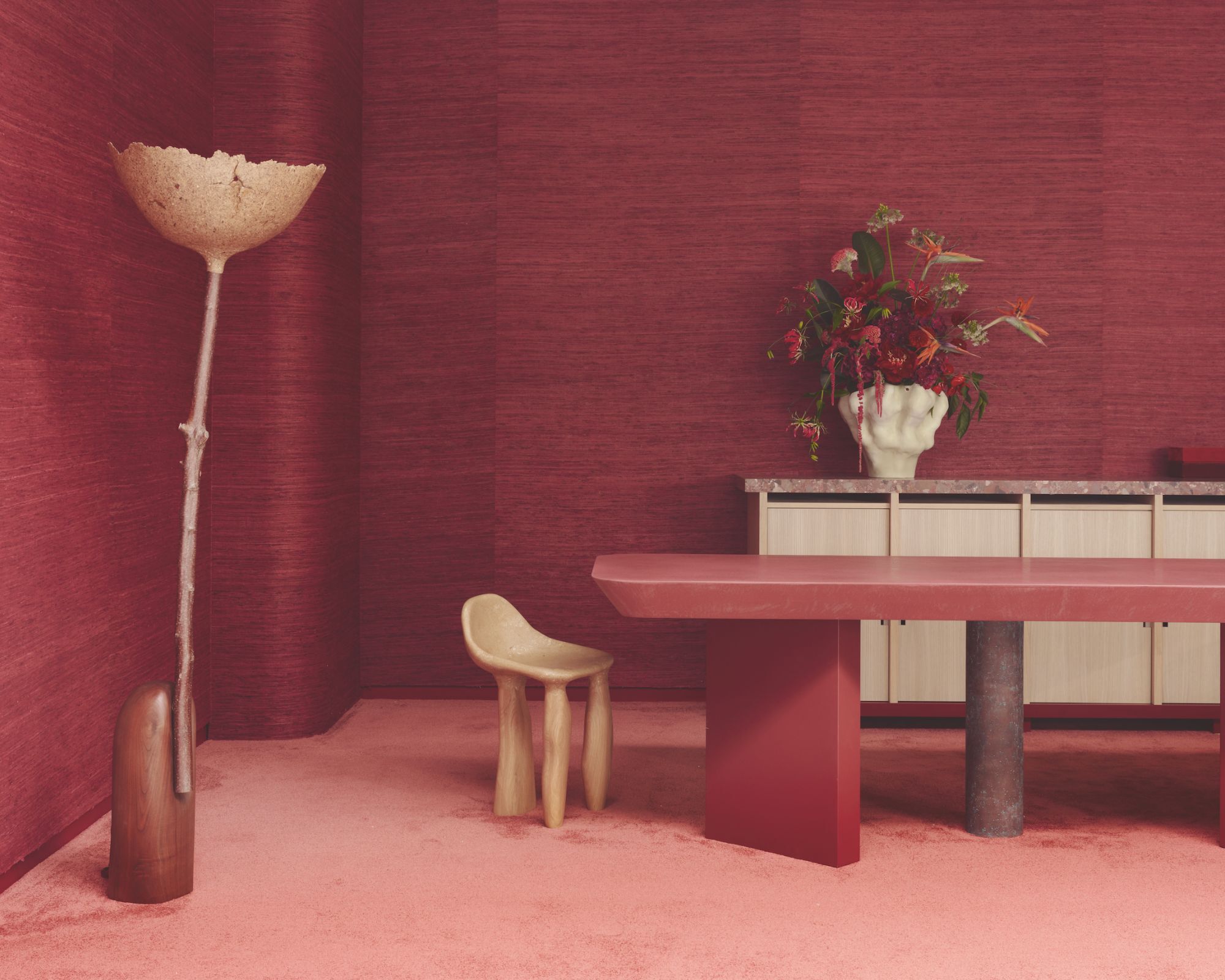 A room with reddish pink carpet, a reddish pink textured wall covering and furniture dotted throughout