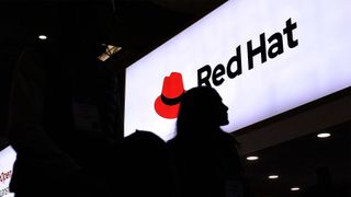 Mobile World Congress (MWC) attendee walks past Red Hat logo and branding pictured on a sign at the company's stall.