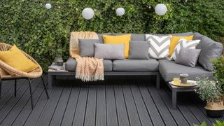 A garden corner sofa in light grey sitting on a freshly painted deck in a dark grey shade