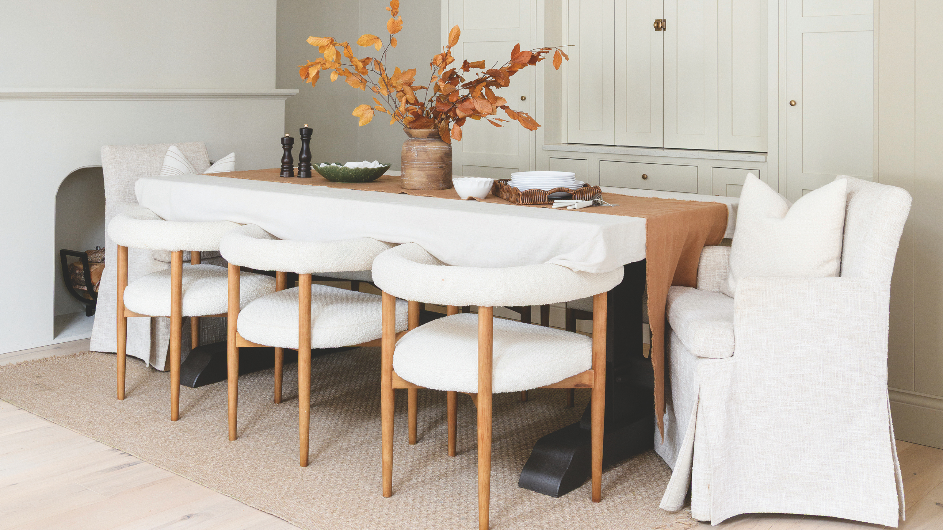 Neural dining table with white boucle dining chairs. Both chairs at the head of the table have a chair skirt.