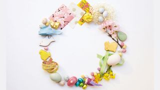 Easter decorations arranged into a wreath shape including Easter eggs, Easter bunnies, spring flowers and greetings cards on a white background