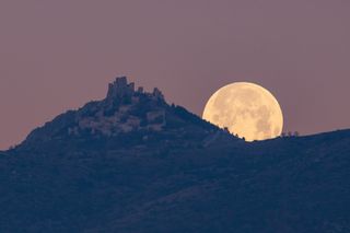 the full moon appears large over a mountain topped by a castle