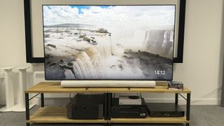 Sonos Arc Ultra soundbar on wooden AV bench beneath TV showing waterfalls on screen