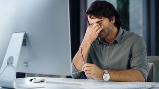 Mature professional business man suffering from a headache while working online on computer checking emails alone at work. One male manager feeling overworked, stressed and tired due to a deadline - stock photo