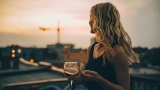 Thoughtful young woman having wine while looking away on terrace during rooftop party at sunset
