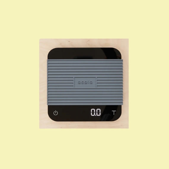 A black digital scale with a textural grey, central rubber swathe sits against a pale yellow background.