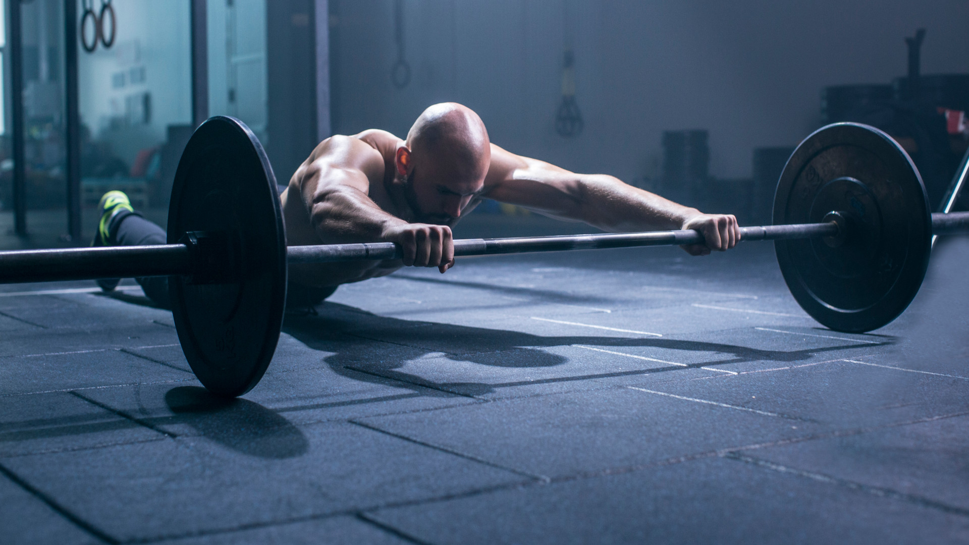 A man performing core exercise 'barbell roll out' at the gym