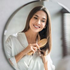 best hair brush - woman smiling in the mirror brushing her hair