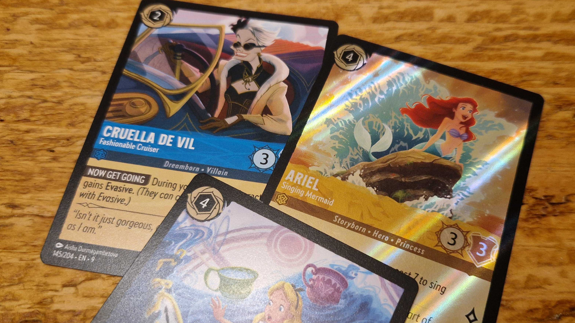 Three Disney Lorcana cards on a wooden surface