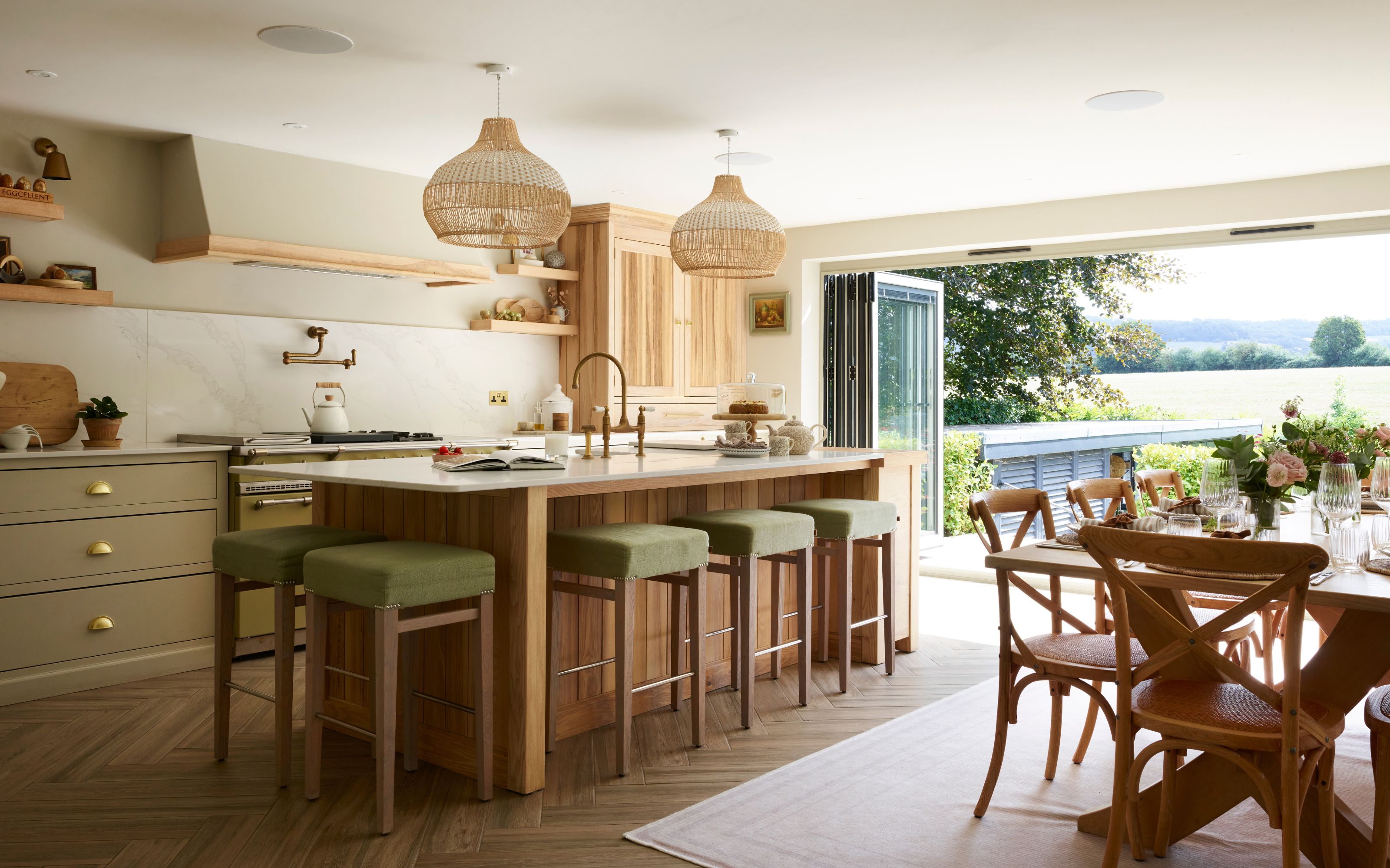 Kitchen diner looking out onto countryside with green kitchen mixed with wooden accents and wooden dining table and chairs