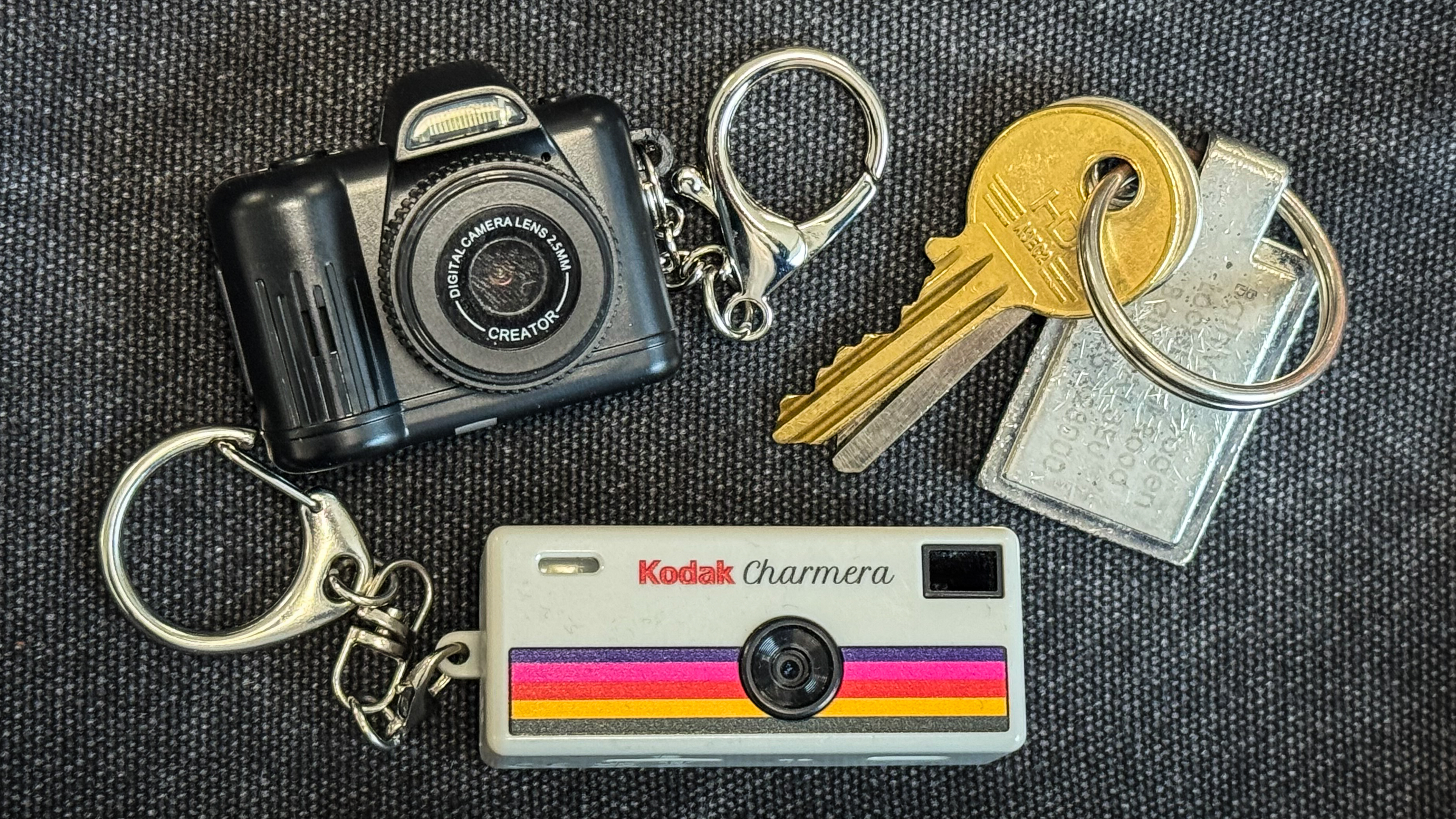 Kodak Charmera and Photo Creator Mini Cam keychain cameras with a set of keys on a dark textured background