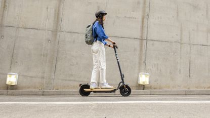 A woman riding the best electric scooter up a hill with a cement wall behind her