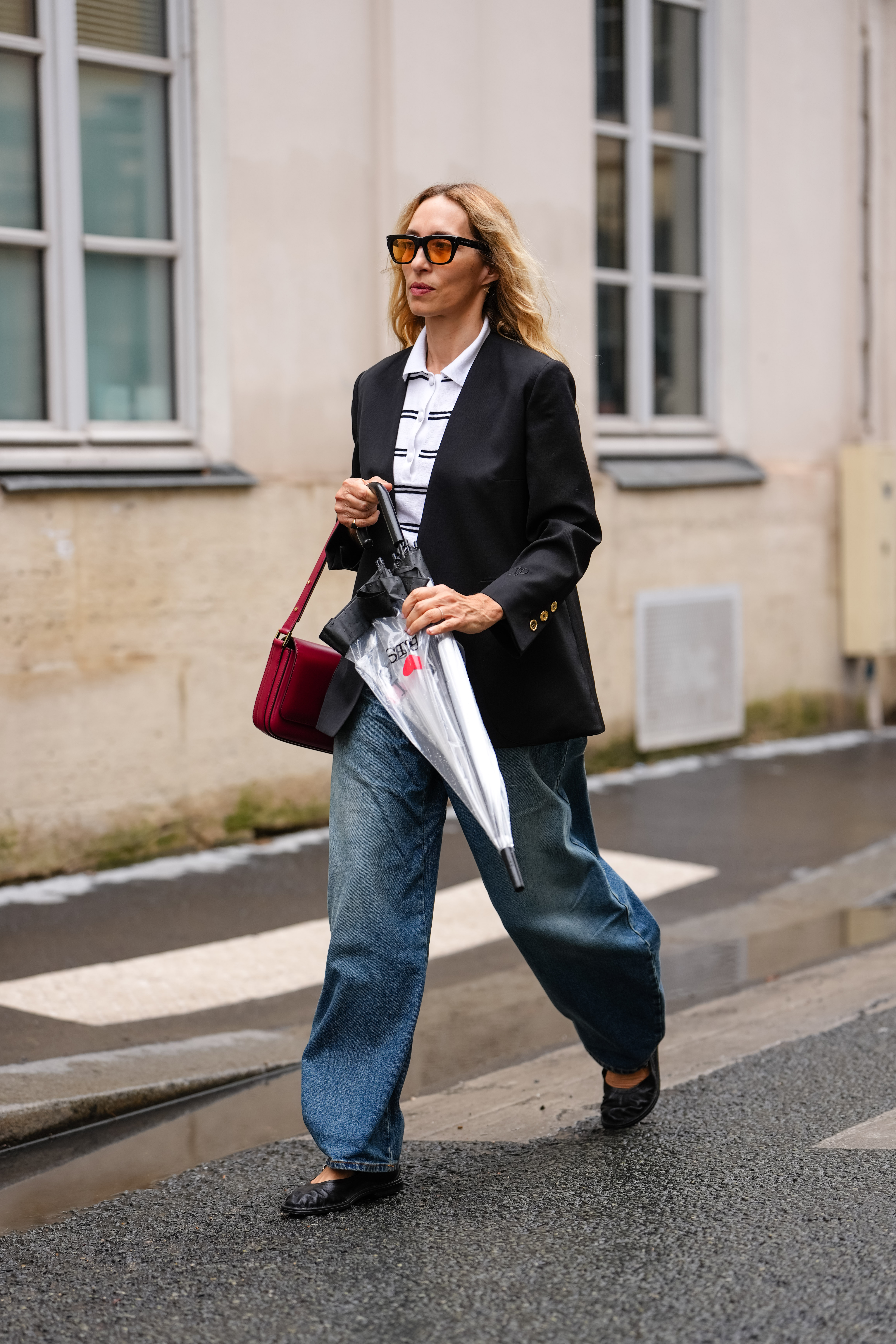 A guest wears a black blazer, white polo shirt, wide-leg blue jeans, and black shoes on June 06, 2025 in Paris, France.