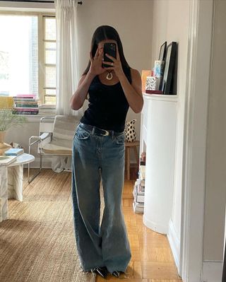 @sasha.mei taking a mirror selfie wearing black tank top, blue jeans, and silver necklace