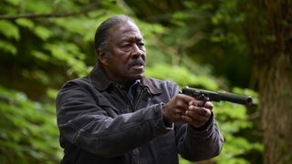 Clarke Peters pointing a gun in a green forest in new thriller Truelove