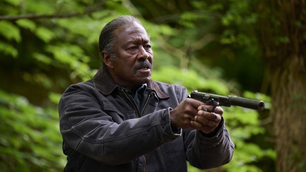 Clarke Peters pointing a gun in a green forest in new thriller Truelove