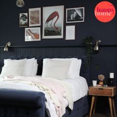 Dark painted panelled bedroom wall, navy blue bedframe, white bedding, hanging wall art, bedside table