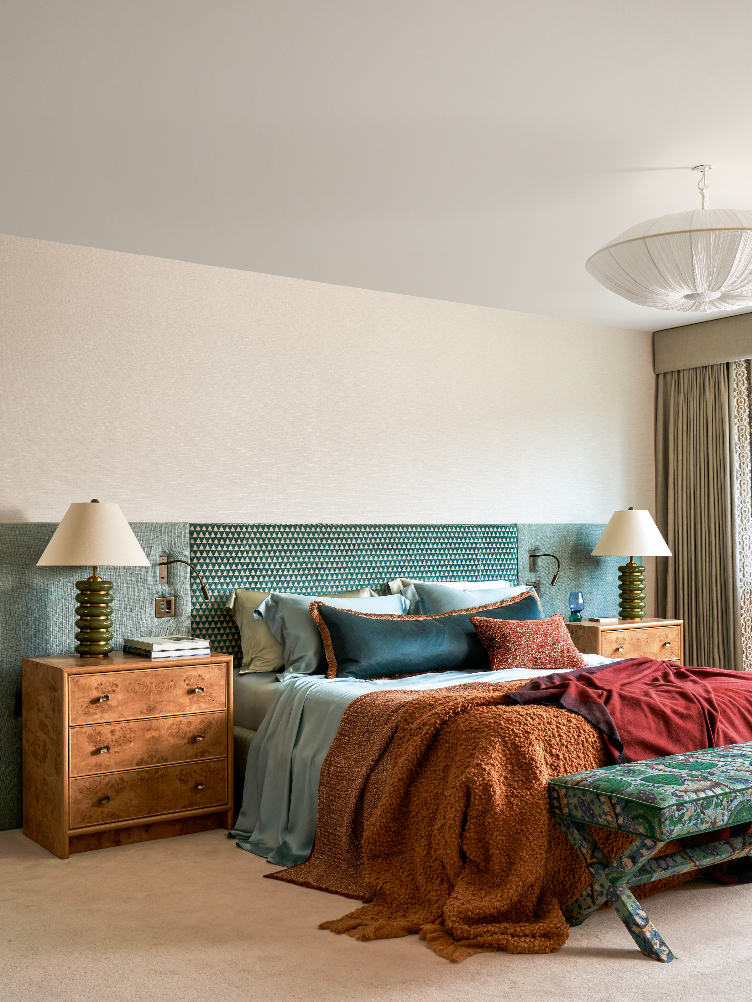Cream bedroom with turquoise extended headboard, burl wood bedside tables and blue and rust bedding