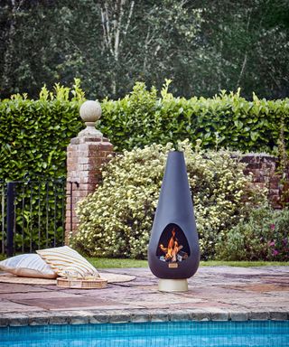 A black chimenea fire pit by pool with circular outdoor area rug and outdoor cushion decor by pool