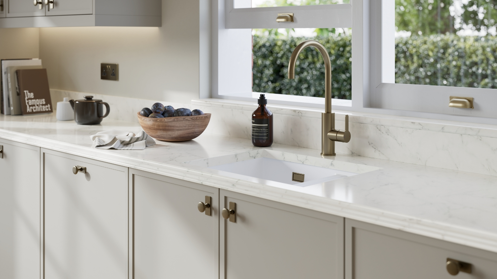 Marble countertop with a brass gooseneck tap, undermounted sink, and a bowl of plums by a window.