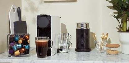 A Nespresso machine and milk frother with pods on a marble kitchen surface