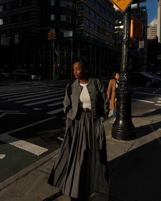 @iamnkirote wears an elegant winter outfit featuring a grey pleated maxi skirt, white top and a cropped wool jacket