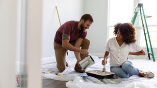 female and male in room being decorated pouring paint into tray with ladder in background