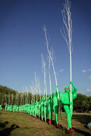 People wearing green suits walking in a line holding a tree each