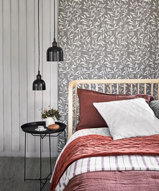 A wooden bed with red and white bedding in front of a grey and white floral wall and two black pendant lamps