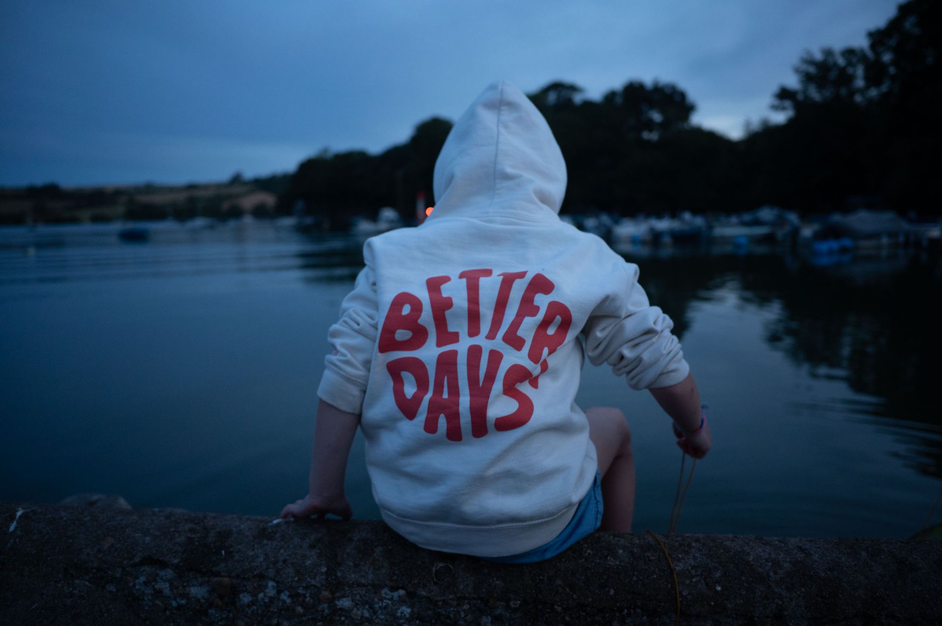 Young child wearing a hoodie side on a riverside wall, crabbing. 