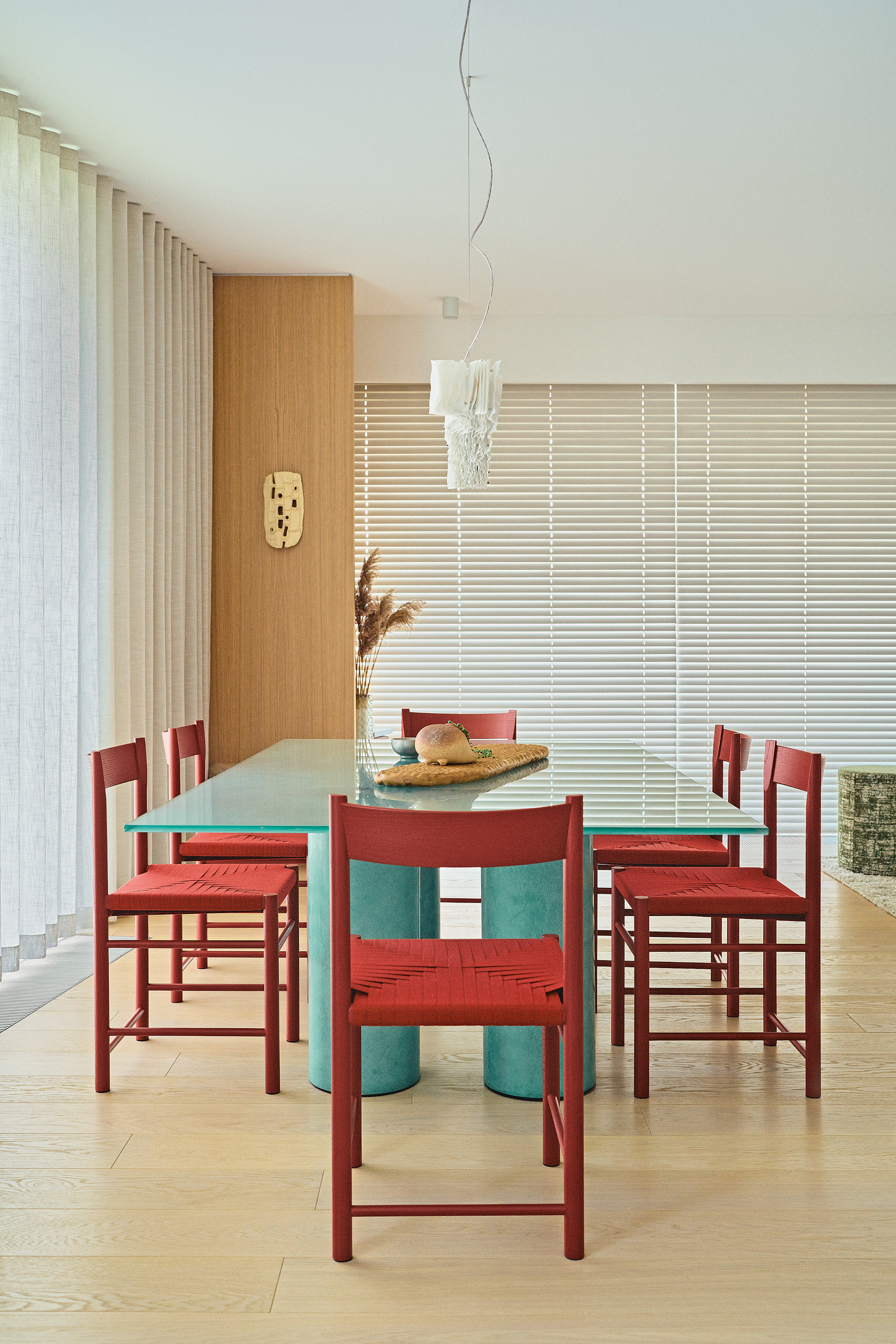 Dining room with white walls, white blinds, wooden floors, teal rectangular dining table and red chairs