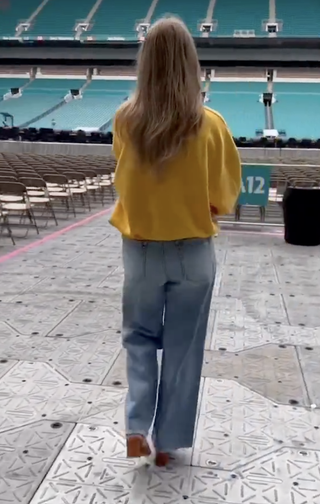 Taylor Swift wears a yellow sweatshirt with wide leg jeans and wedge sandals in a video