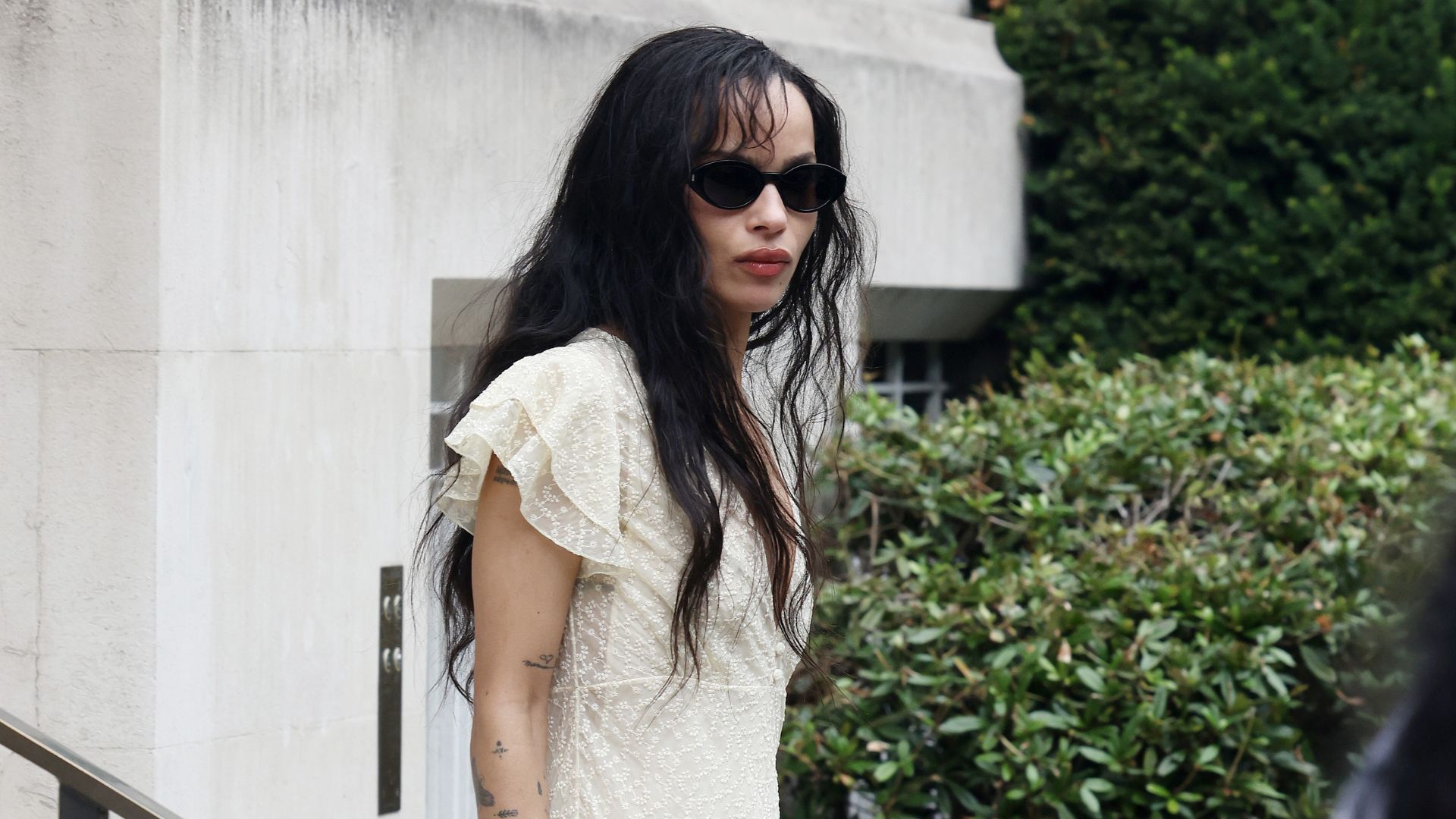 Zoe Kravitz walks down steps outside wearing a butter yellow dress with black ballet flats and a YSL handbag.
